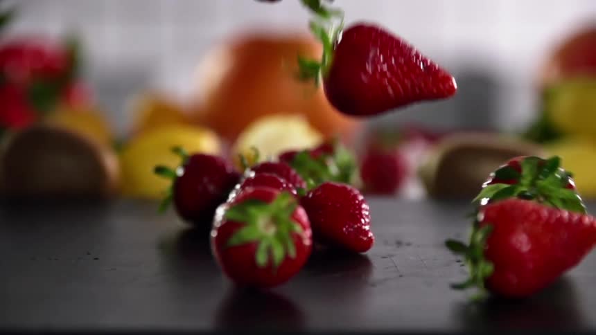 Fresh red strawberries fall on the countertop with fruits in the background