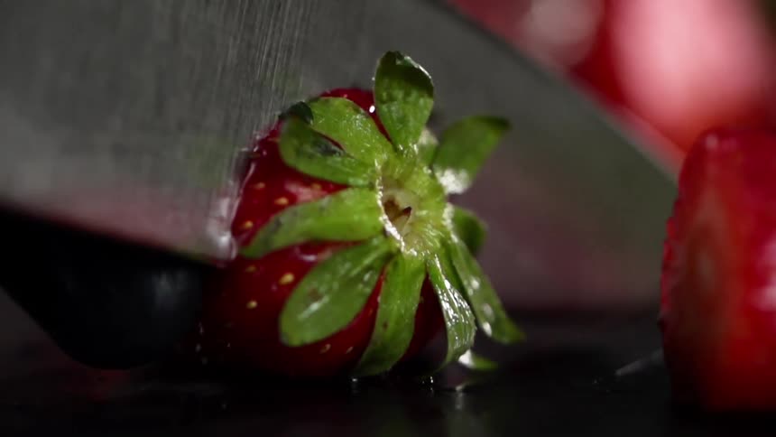 Hand wearing black latex glove uses thumb and forefinger to gently secure strawberry then slices the calyx off of the top