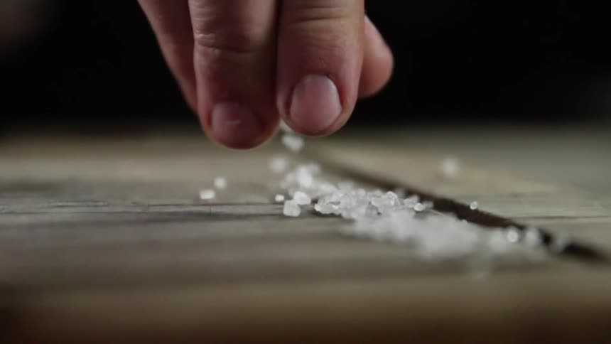 Close up of a man sprinkling grains of salt over a wooden board