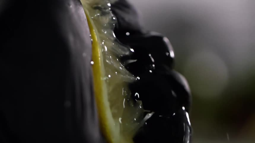 Close up of a hand with black glove squeezing a juicy lemon