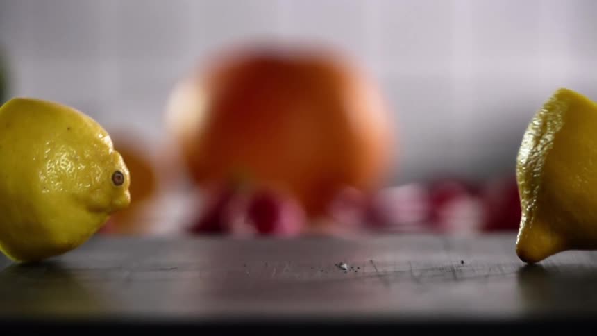 A lemon sliced in half drops on a wooden table and falls apart
