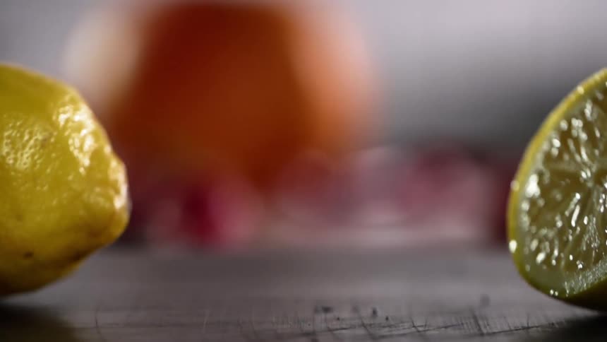 Two halves of a lemon fall onto a wooden table