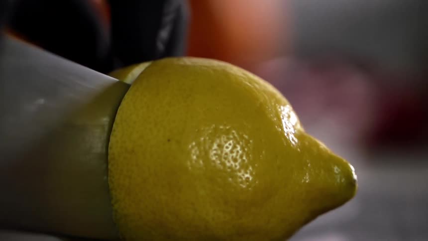 A person wearing black gloves slices through a lemon with a knife