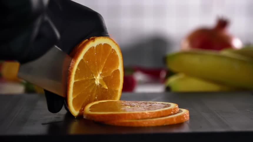 A person wearing black gloves cuts an orange with a knife