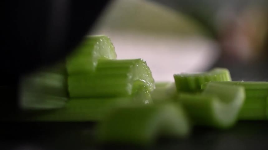 The cook wearing black gloves cuts a stick of celery