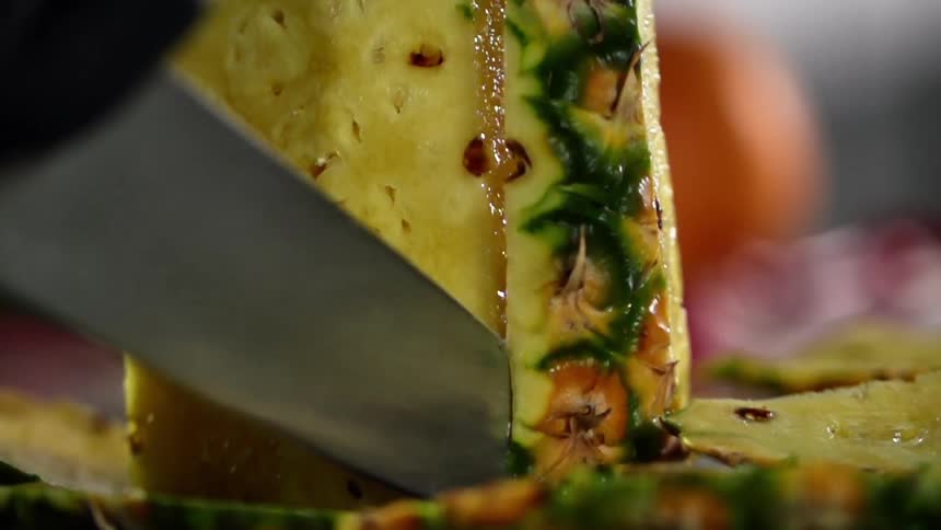 Chef wearing black latex gloves cuts a pineapple with a sharp kitchen knife