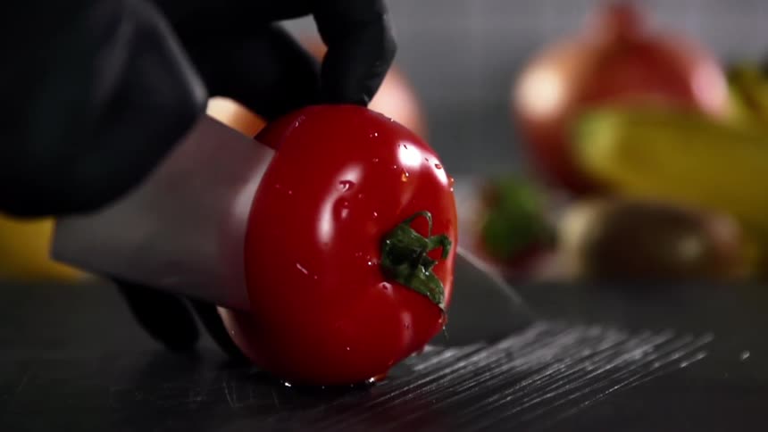 Close up of hands wearing black gloves cutting a tomato in half