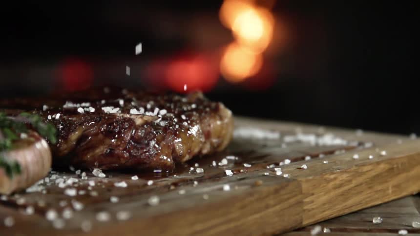 Salt drops over a cooked meat patty sitting on a cutting board