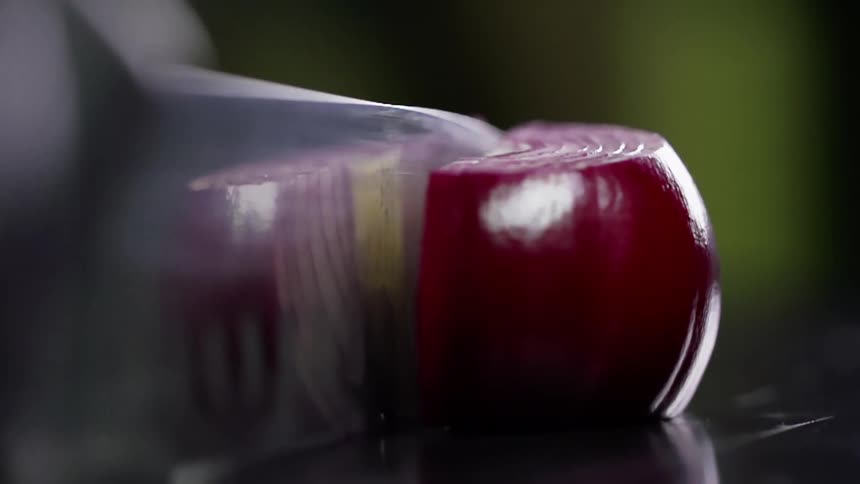 A knife chops a red onion in half
