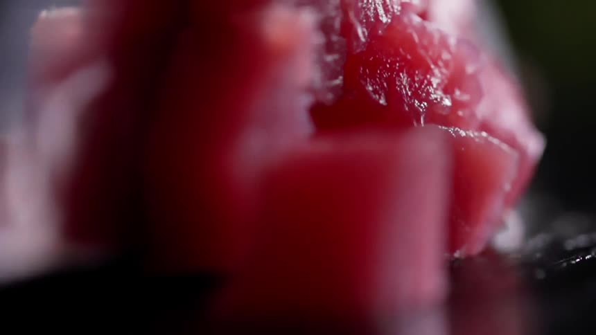 Close up of a sharp knife cutting meat into cubes