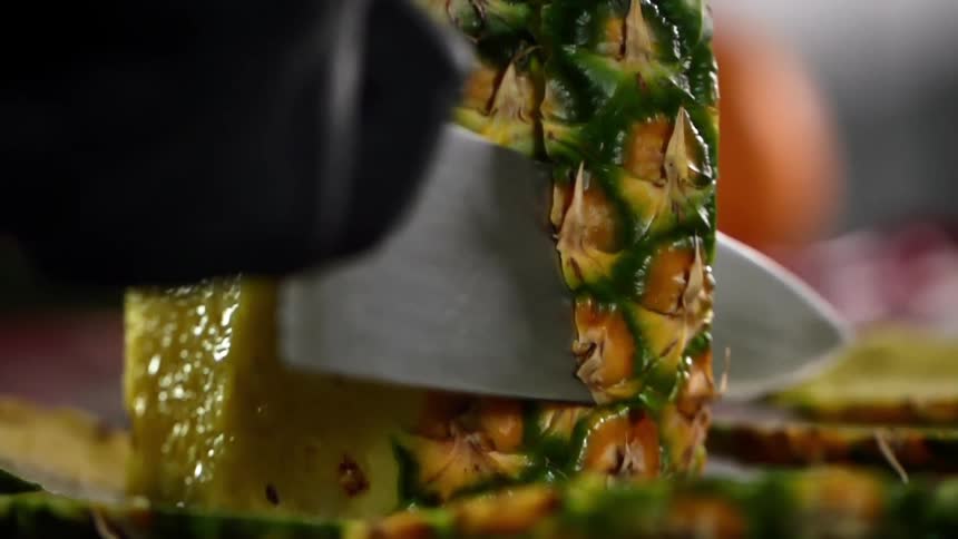 A black gloved hand cuts a pineapple with a knife