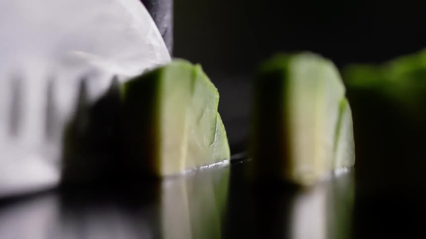 A sharp knife is used to cut pieces of avocado into smaller slices