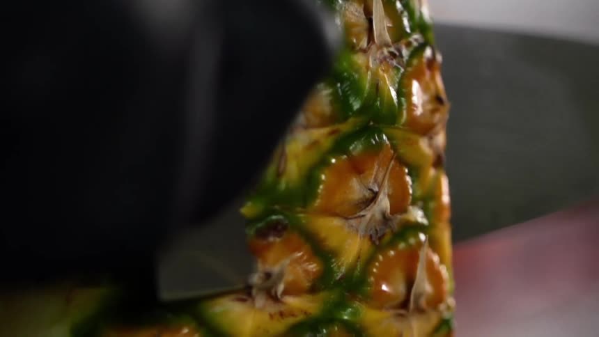 A person wearing a black glove slices pineapple with a knife