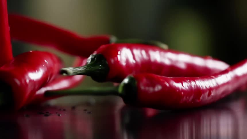 A bunch of red pepper are dropped onto a dark reflective surface