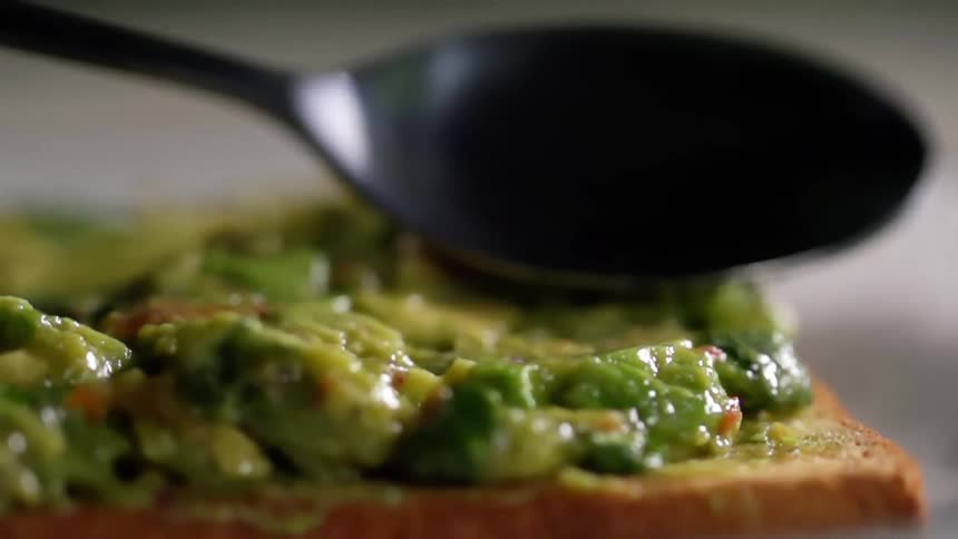 The back of a spoon is used to smooth guacamole on toast