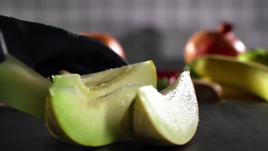 The cook wearing black gloves slices a melon