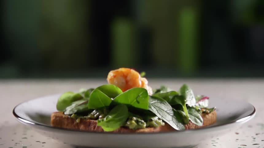 A piece of shrimp drops on a bed of greens sitting on a piece of bread