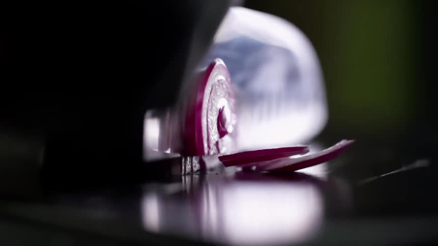 Sharp chef knife slicing a red onion in slow motion