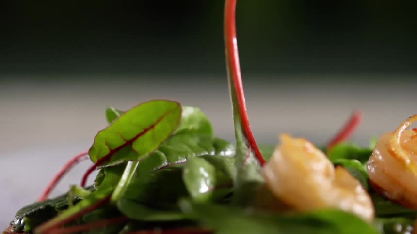 Several pieces of grilled shrimp are dropped on top of a pile of leafy produce