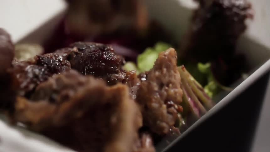 Pieces of meat fall over vegetables inside an asian food takeout cardboard box
