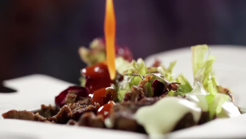 Dressing or sauce is being poured onto a plate with salad and meat