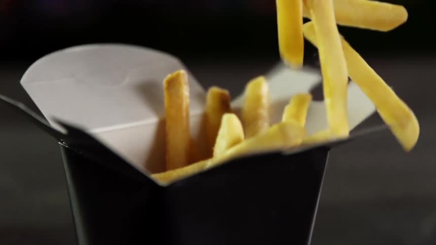 French fries are dropped into an open takeout container with dark sides