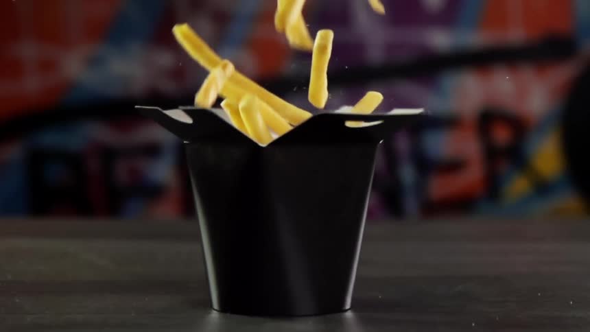 French fries falling into a black take out box in slow motion