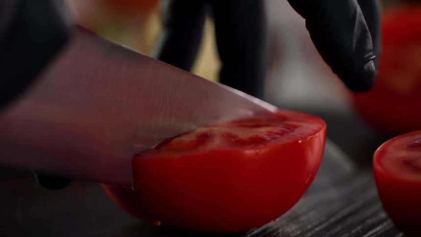 Close up of hands wearing black gloves cutting a tomato in half with a sharp knife