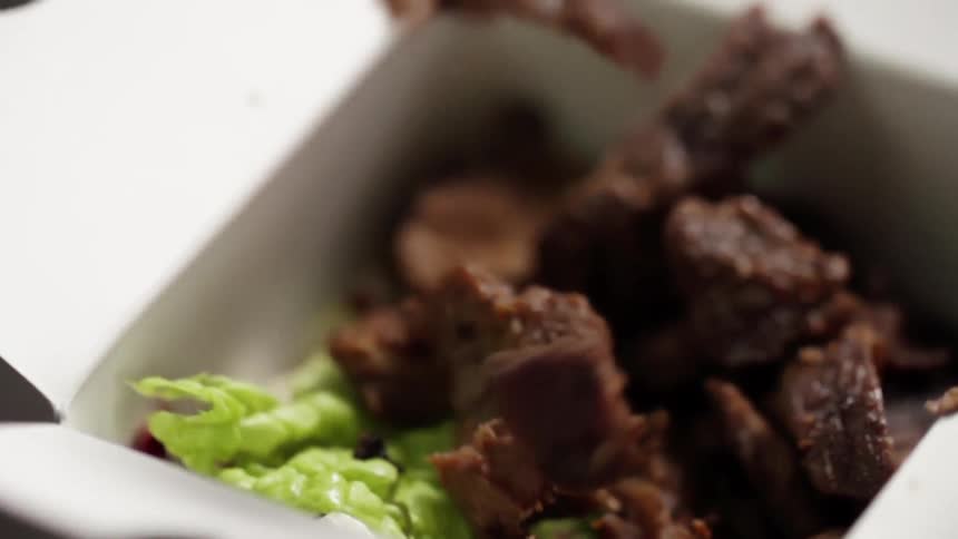 Beef pieces dropped into takeout box on top of lettuce