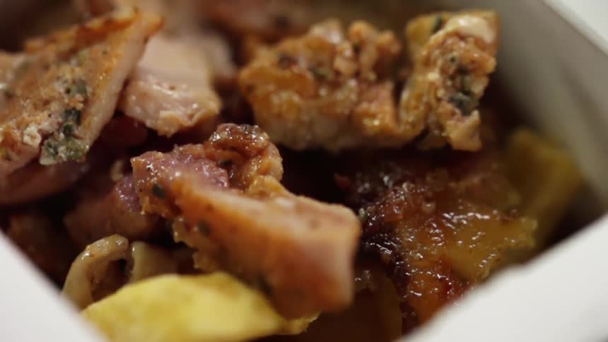 Chunks of meat drop on a pile of french fries in a meal box