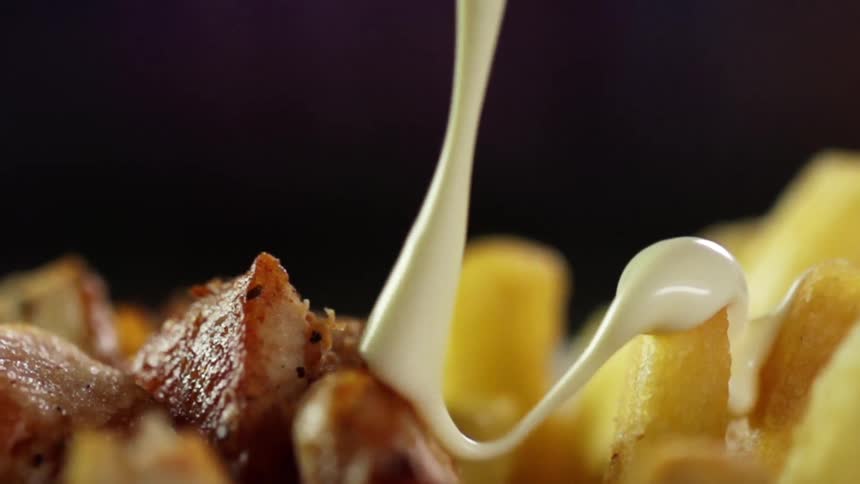A yellow sauce pours over french fries and chunks of meat