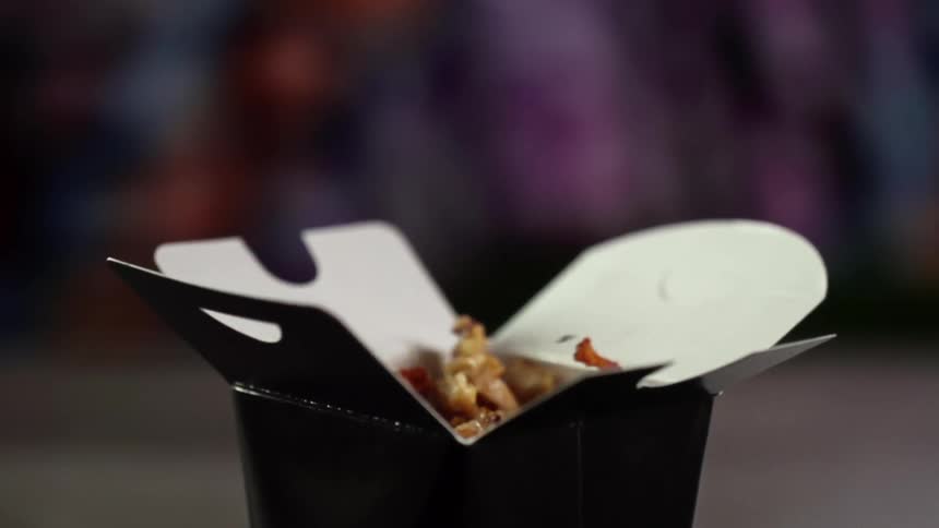 Several pieces of cooked chicken are dropped into an open disposable takeout box