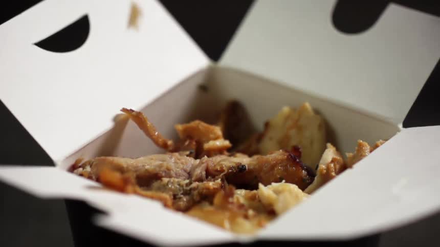 Pulled pork falling over cooked yellow rice inside a cardboard takeout box