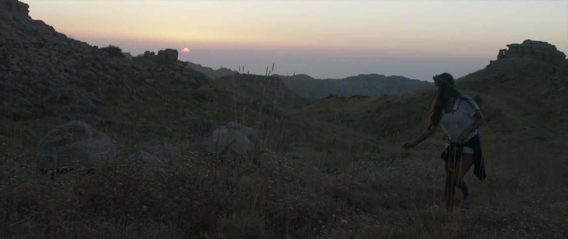 A woman is hiking over some hills at sunset