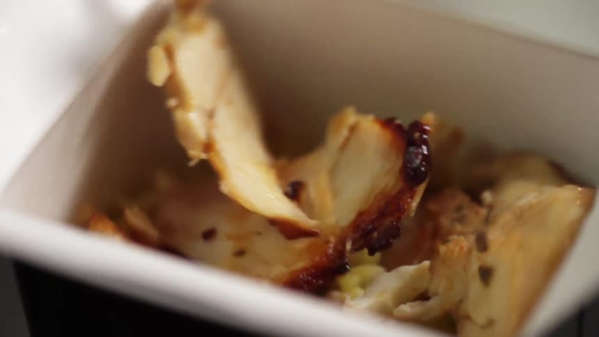 Chicken pieces dropping on a bed of rice in a box container in slow motion