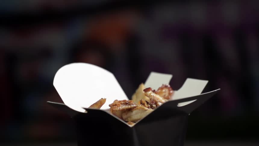 An open takeout box is filled with food that is poured from up above