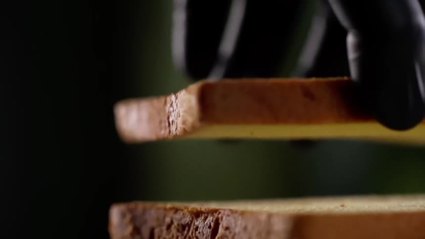 Chef wearing black latex gloves picks up a slice of bread from a pile