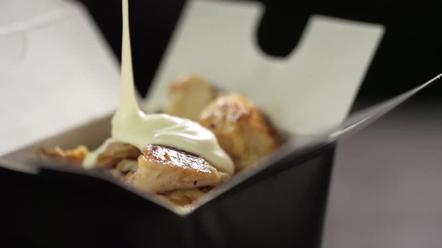 Sauce being put on chicken in a take out box