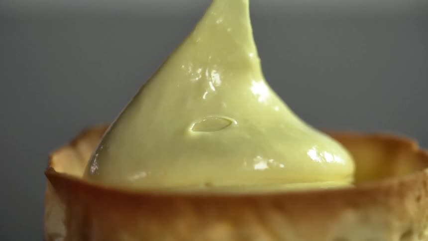 A dollop of creamy sauce is slowly placed onto the top of a pastry