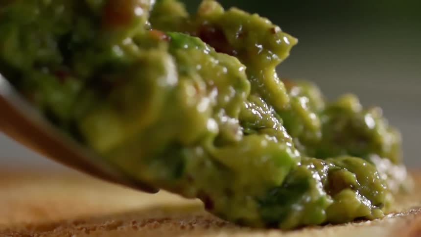 Serving green fresh guacamole with a spoon over toast
