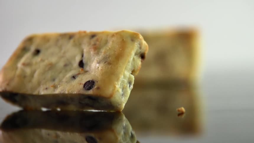 Square pastries filled with chocolate chips falling over a reflective surface