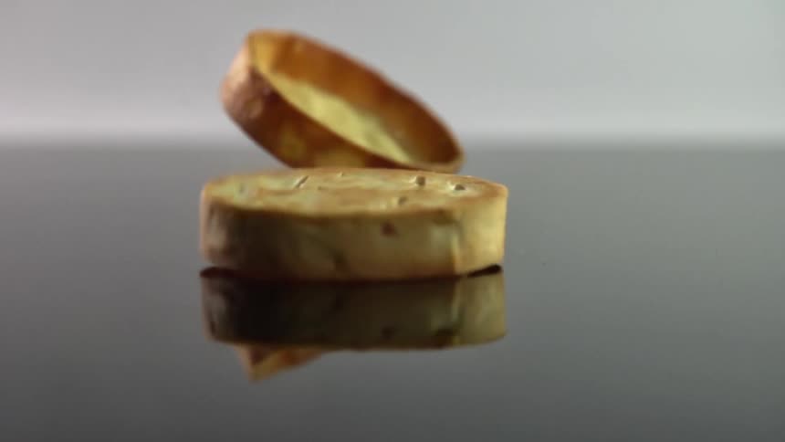 Empty pastry shells rotate on dark reflective surface before falling to lay flat