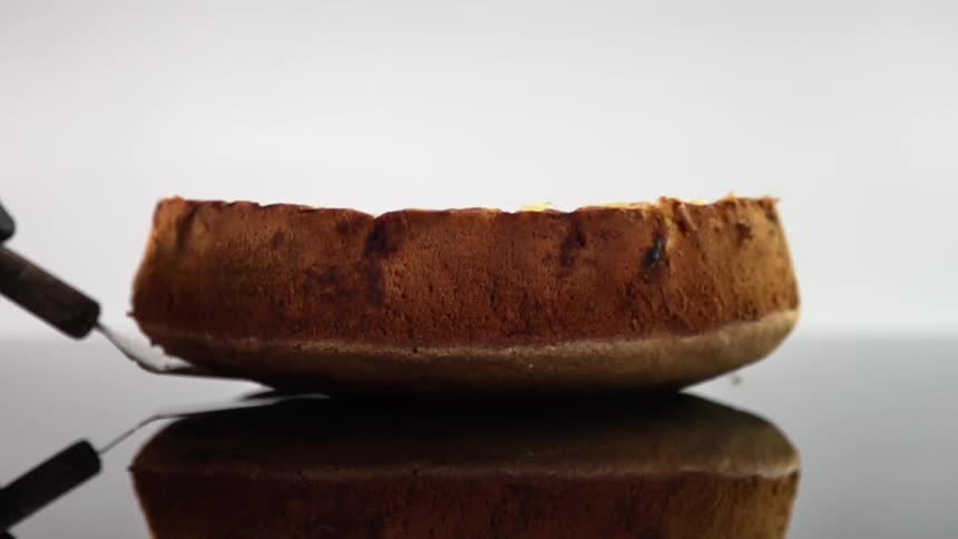 A cake is slowly lowered onto a table with a spatula