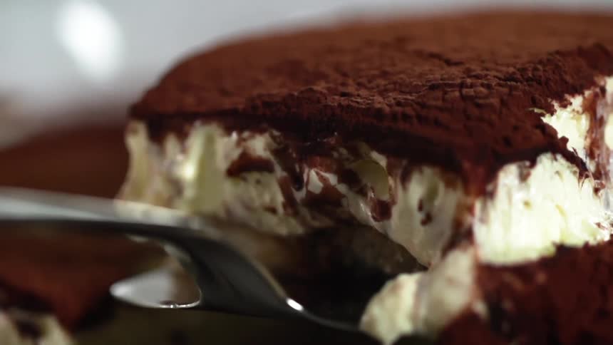 A piece of chocolate cake with cream is lifted up