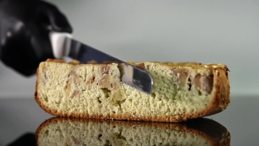 Chef wearing black latex glove cuts a pie with a serrated kitchen knife over a reflective surface