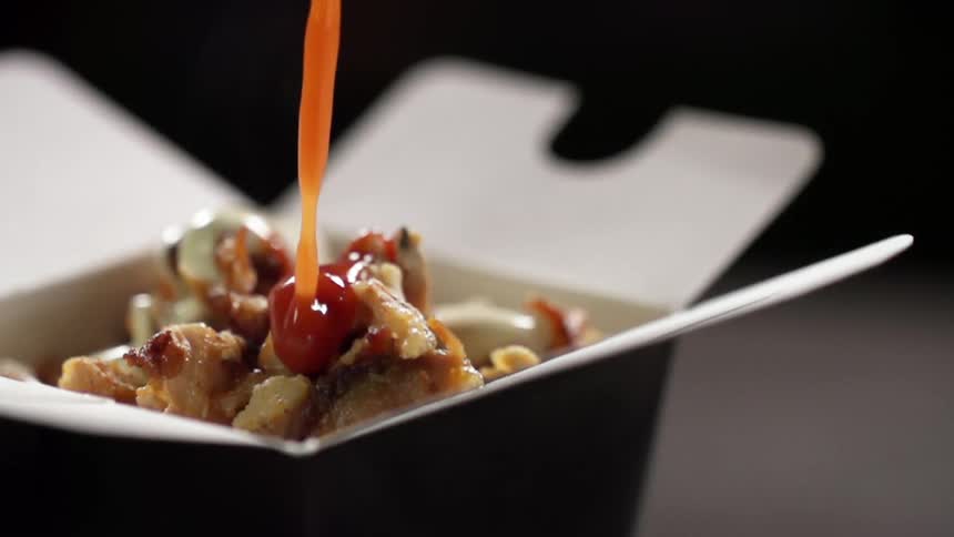 A red sauce is added to a container of chinese takeout