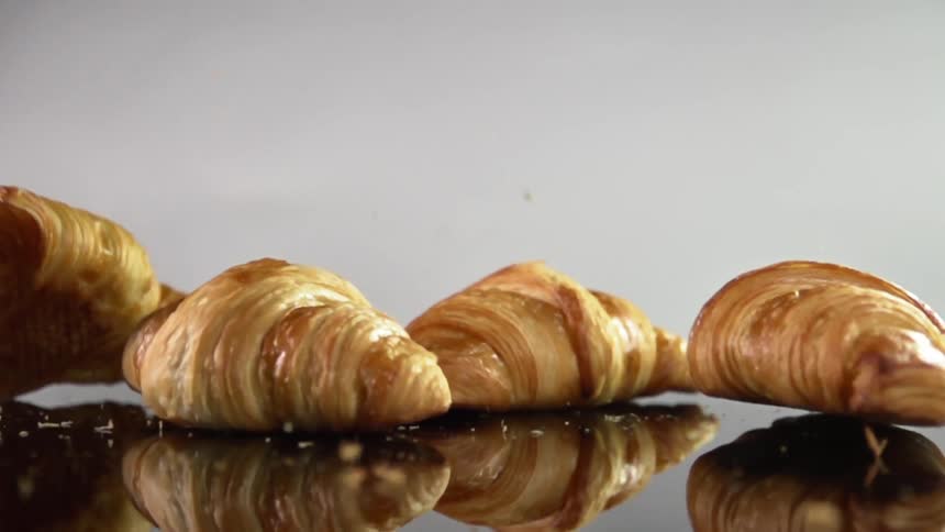 Croissants falling over a reflective surface leaving crumbs all around