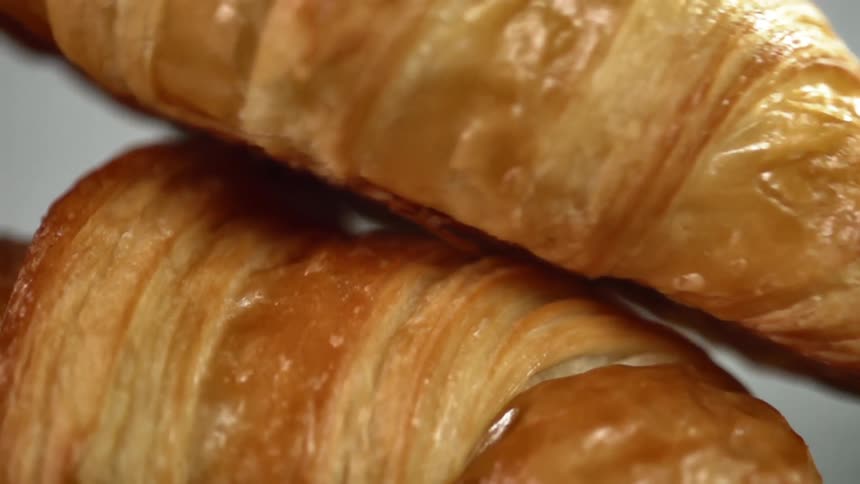 A glazed croissant slides off the top of another croissant