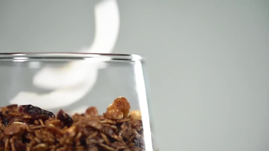 Shaved coconut falls into a glass of granola