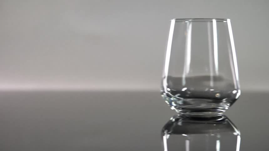 An empty glass is slid across a smooth reflective surface and subtly wobbles as it glides
